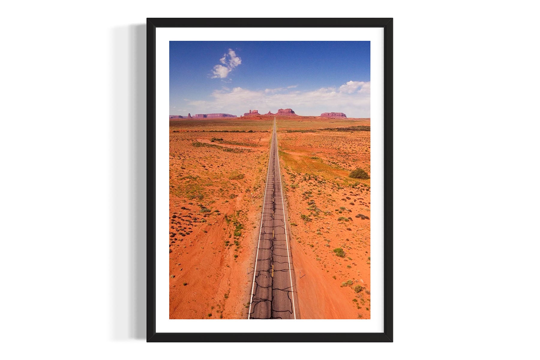 Framed aerial photograph of a desert landscape with a long straight road in Monument Valley by Evan Reinheimer.