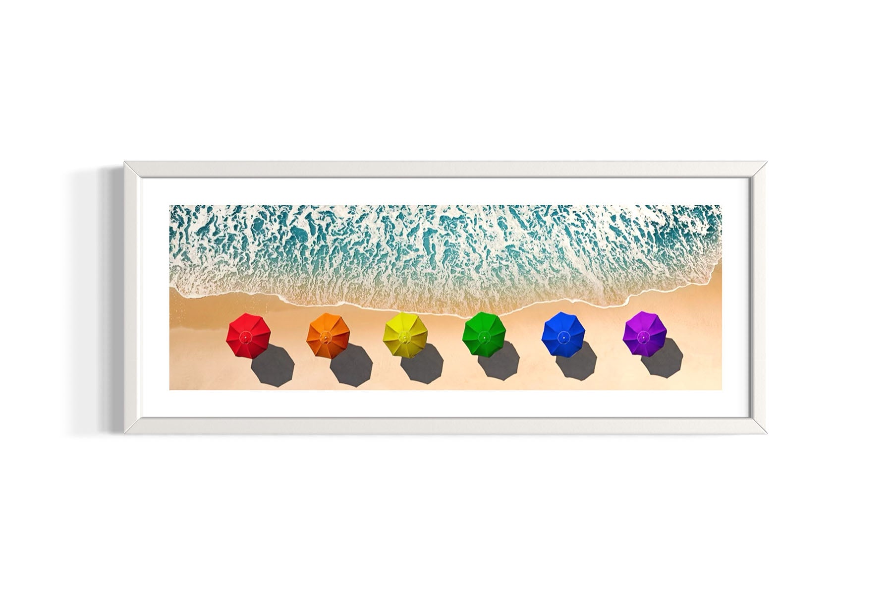 Framed aerial photograph of colorful umbrellas in a rainbow pattern on a beach on Fire Island, NY with ocean waves by Evan Reinheimer.