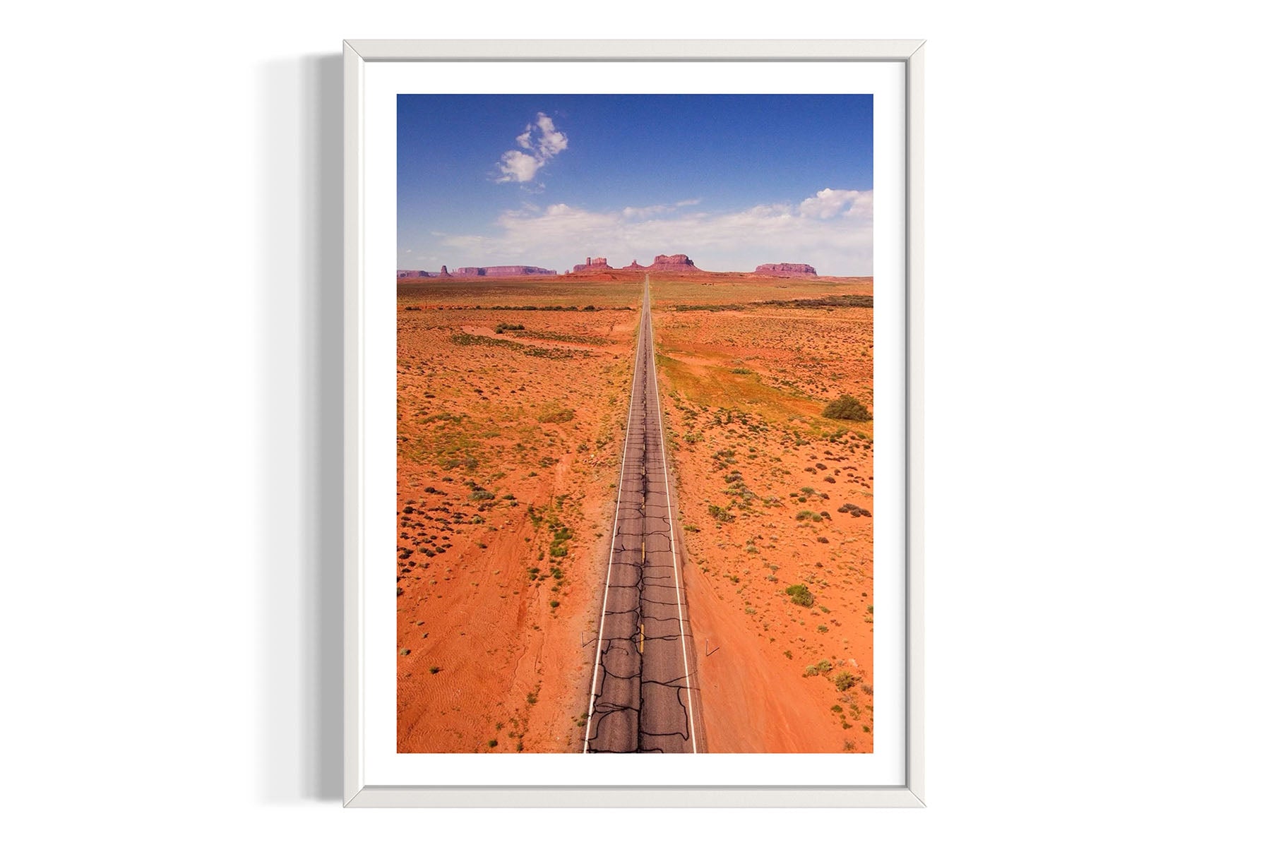 Framed aerial photograph of a desert landscape with a long straight road in Monument Valley by Evan Reinheimer.