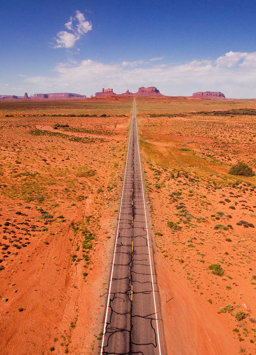 Aerial photograph of a desert landscape with a long straight road in Monument Valley by Evan Reinheimer.