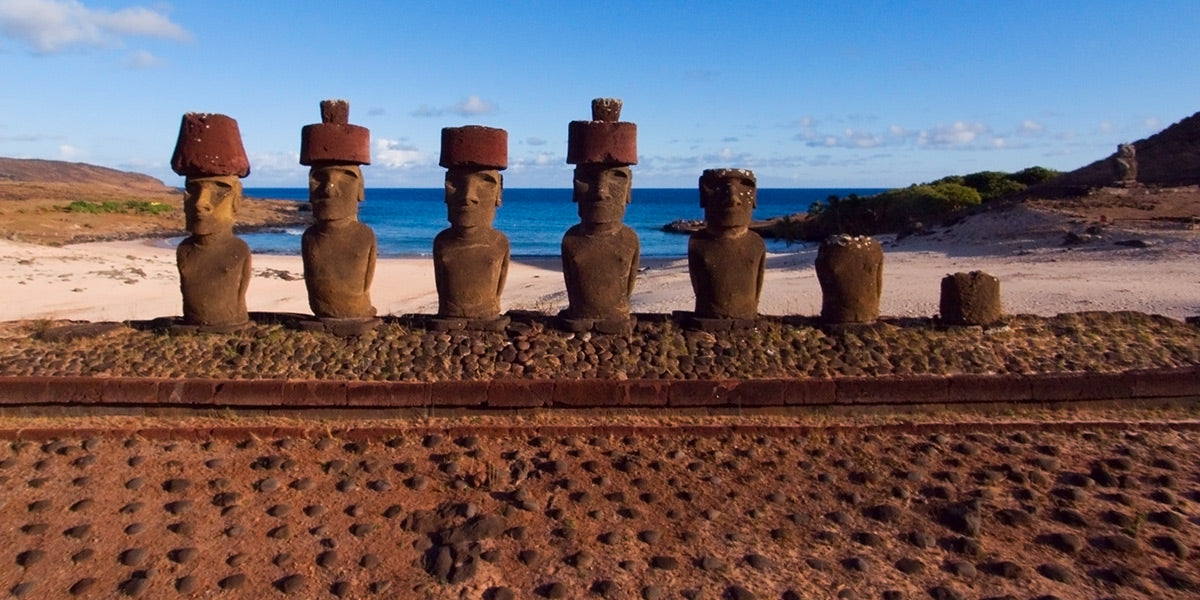 Photograph of stone Moai statues on an Easter Island beach with ocean and sky in the background.
