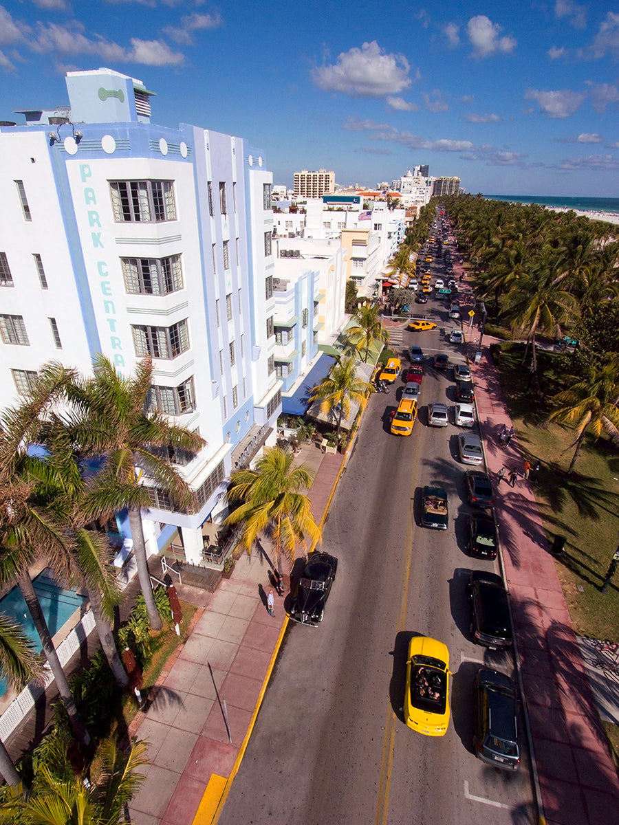 Aerial photograph of Ocean Drive in Miami Beach, FL with buildings, cars, and palm trees by Evan Reinheimer.