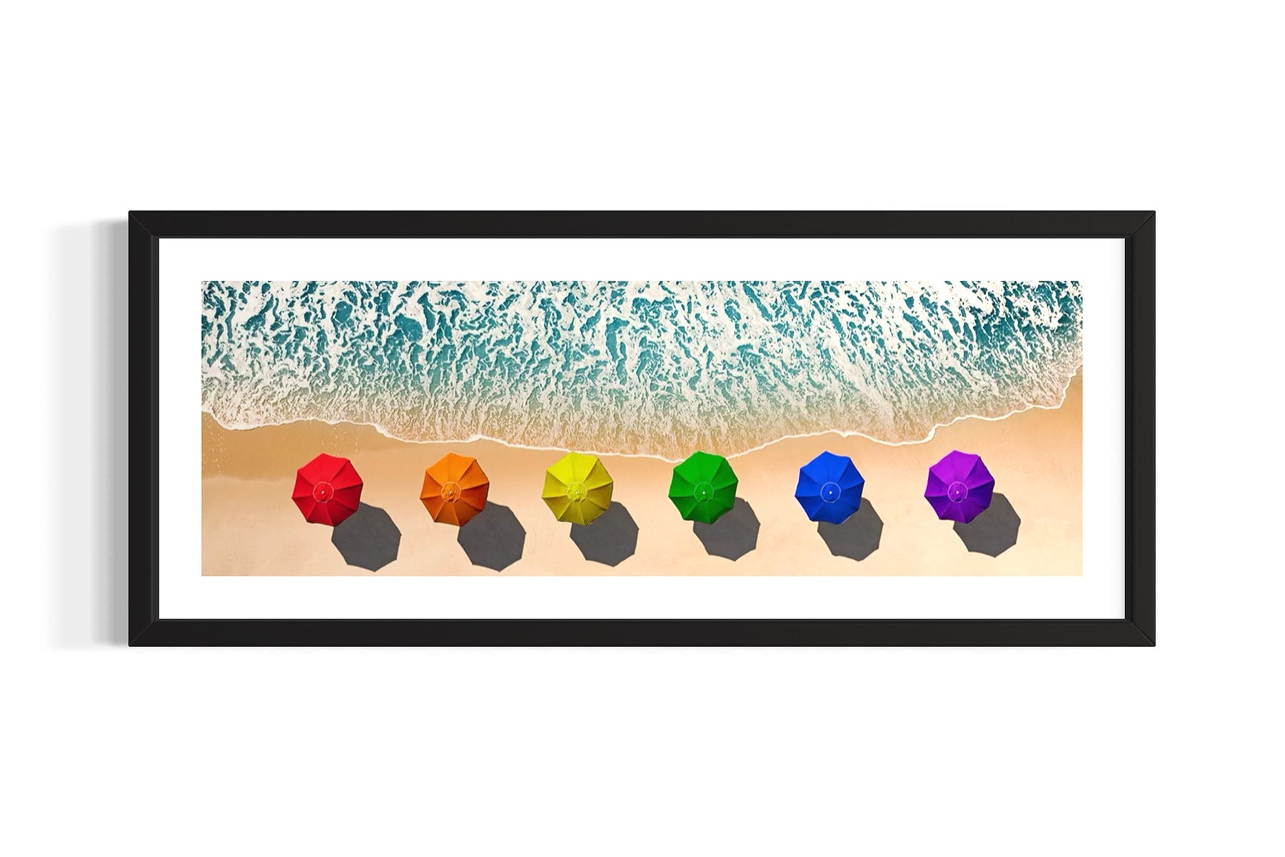 Framed aerial photograph of colorful umbrellas in a rainbow pattern on a beach on Fire Island, NY with ocean waves by Evan Reinheimer.