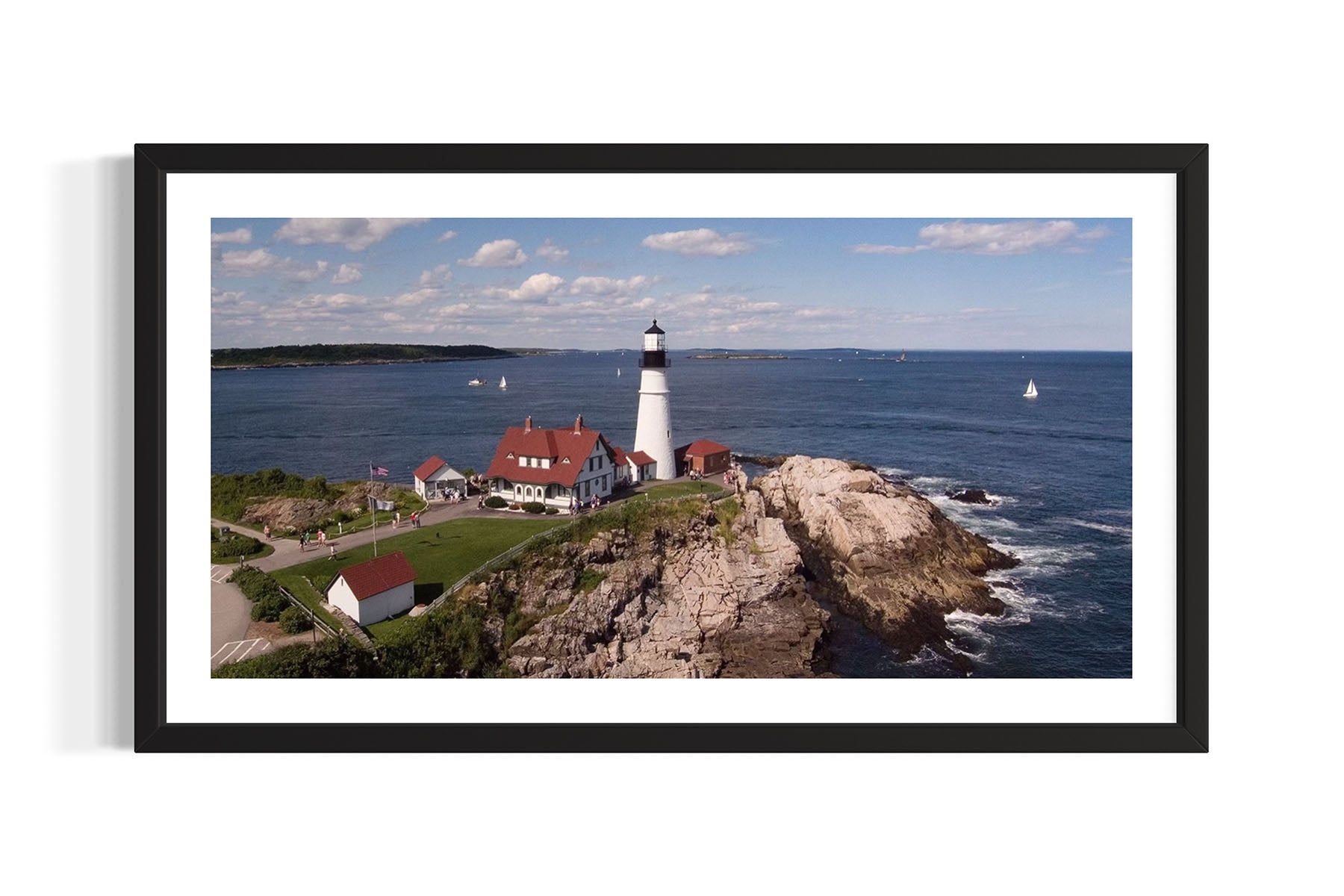 Framed aerial photograph of the Portland Head Light lighthouse on a rocky island with ocean and sky in the background by Evan Reinheimer.