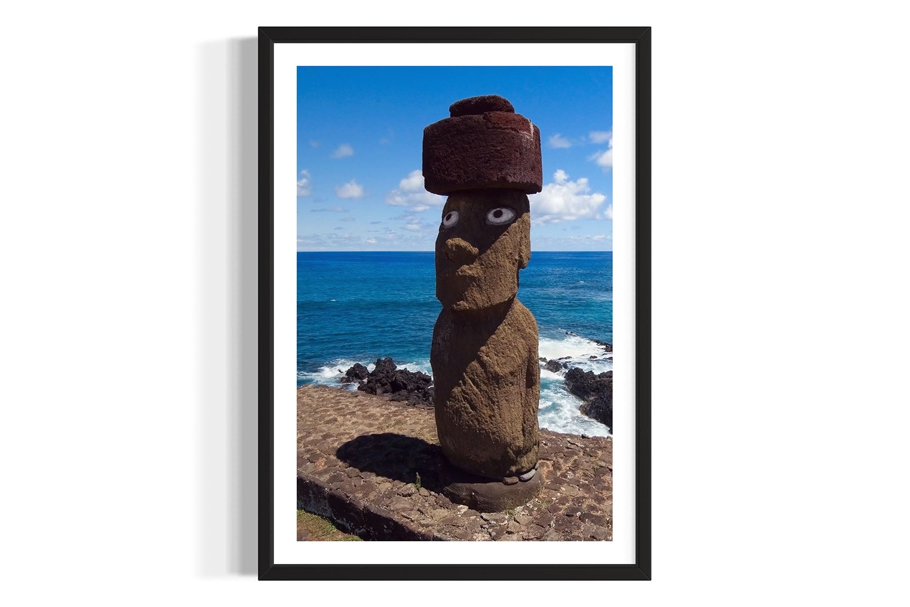 Framed aerial photograph of a Moai stone statue with a hat against a coastal background on Easter Island by Evan Reinheimer.