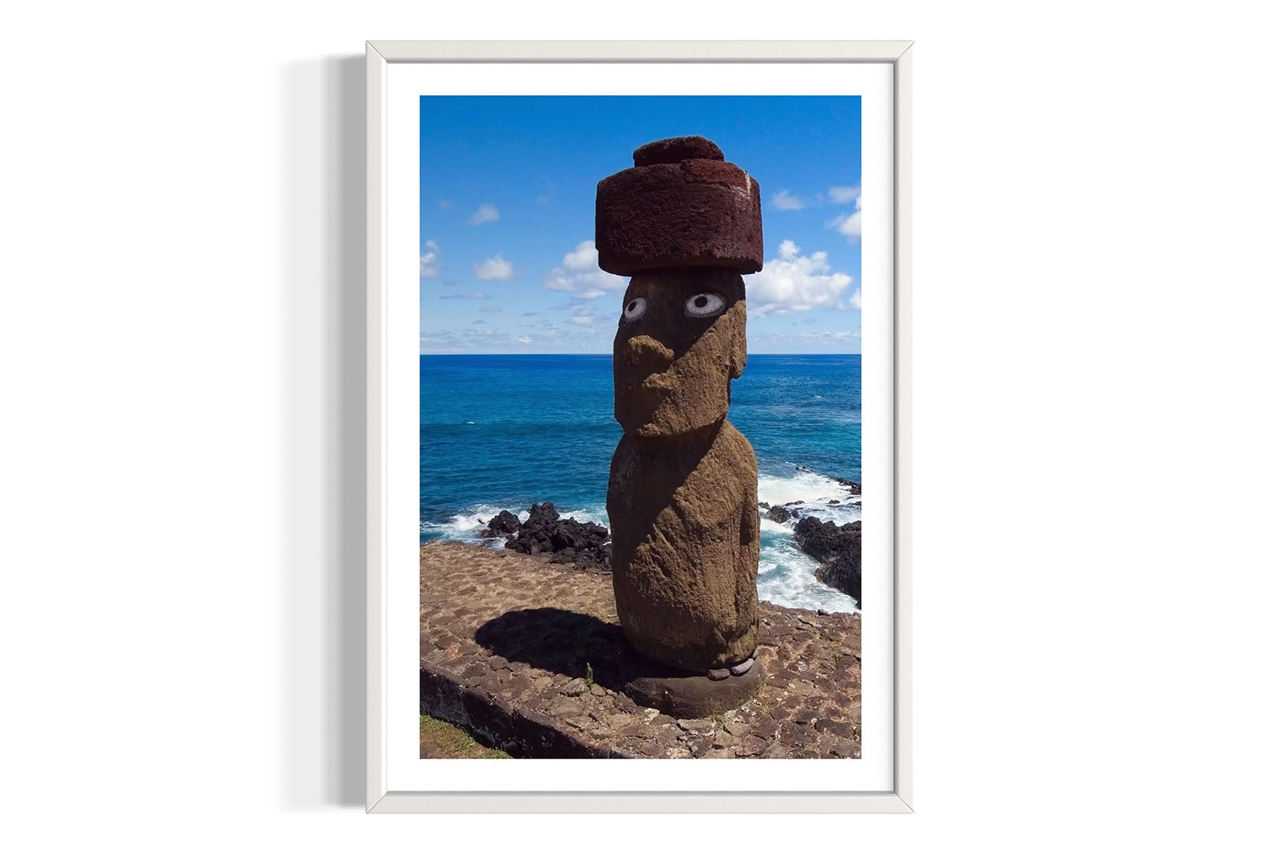 Framed aerial photograph of a Moai stone statue with a hat against a coastal background on Easter Island by Evan Reinheimer.
