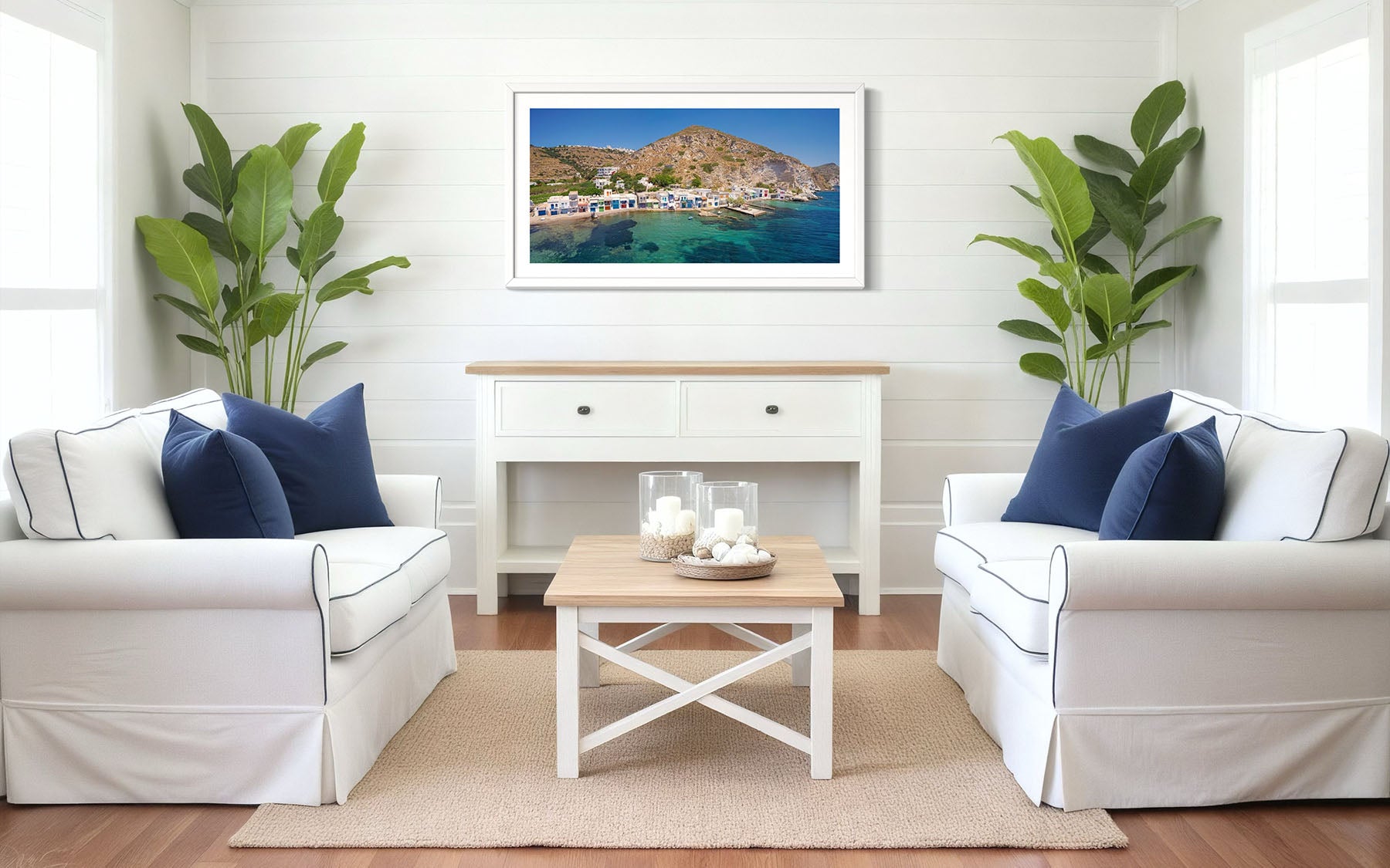 Living room with white sofas, blue pillows, a coffee table, and a framed picture of a coastal scene by Evan Reinheimer.