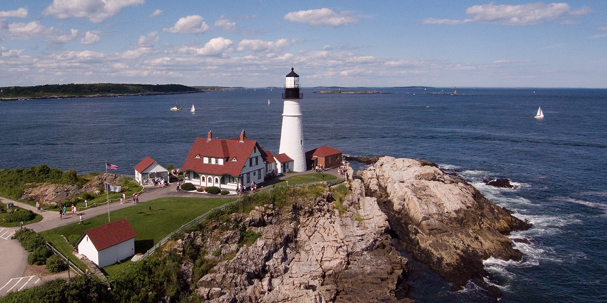 Aerial photograph of the Portland Head Light lighthouse on a rocky island with ocean and sky in the background by Evan Reinheimer.